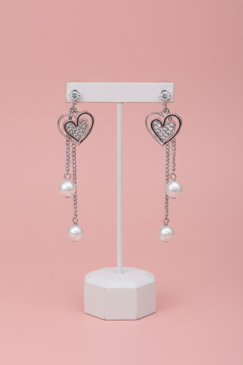 Silver heart drop earrings on display stand blush pink background